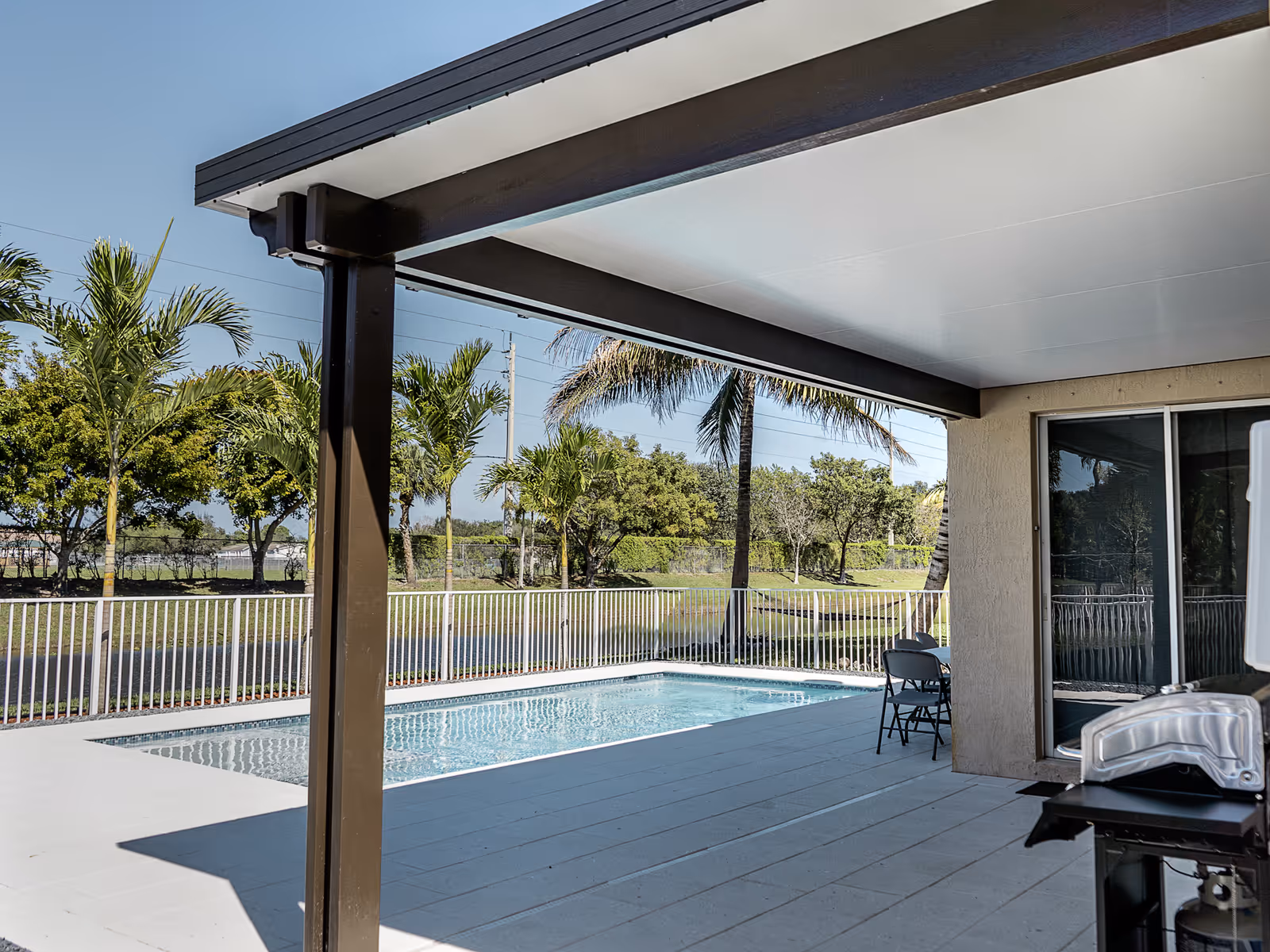 Aluminum patio cover beside a pool with palm trees in South Florida